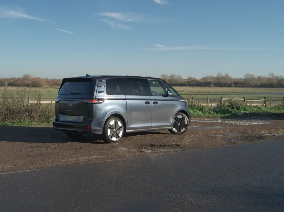 A grey Volkswagen ID. Buzz electric people carrier parked beside a country road under a blue sky.